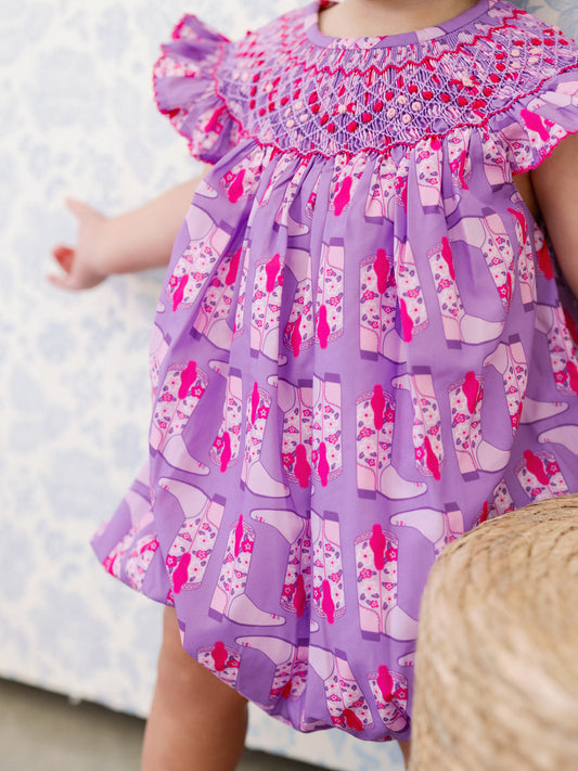 Child wearing a purple dress with pink cowboy boot pattern on a light blue background
