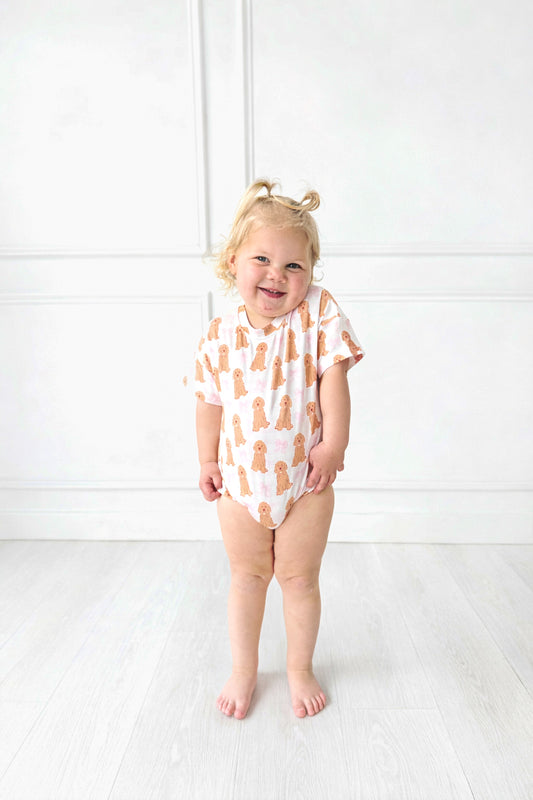 Child wearing pink t shirt bubble with golden doodle dogs on it standing in front of white background.