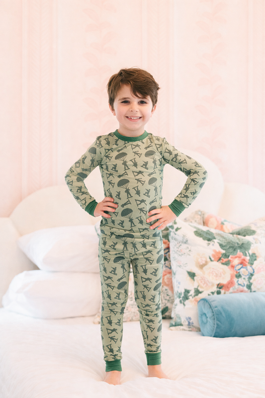 Child wearing a green pajama set with a green army manpattern, standing in a bedroom.