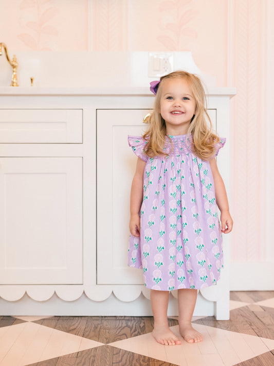 Young girl in a pink floral dress standing in a room with a white fireplace.