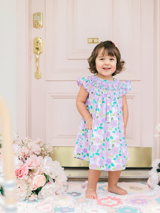 Child wearing a floral dress standing in front of a decorative door with flowers and candles.