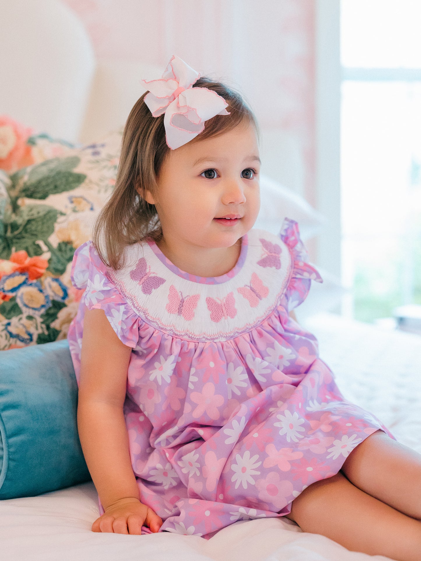 Young girl wearing a pink butterfly dress sitting on a couch.