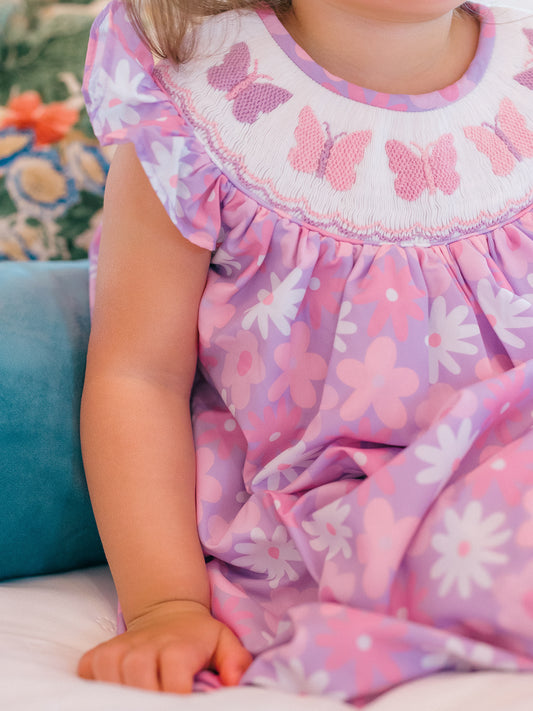Child wearing a pink dress with butterfly patterns sitting on a couch.
