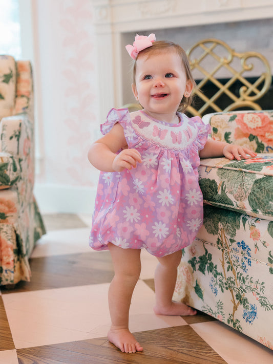 Child in a pink butterfly floral dress standing in a room with floral furniture.