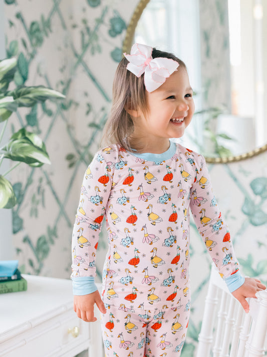 Child wearing a colorful cartoon goose pajama set with a white bow in a room with greenery.