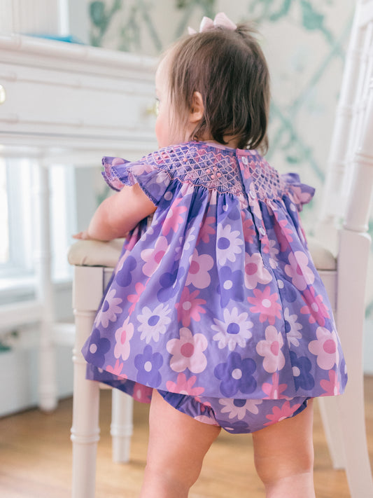 Child wearing a floral diaper cover set standing on a chair indoors.