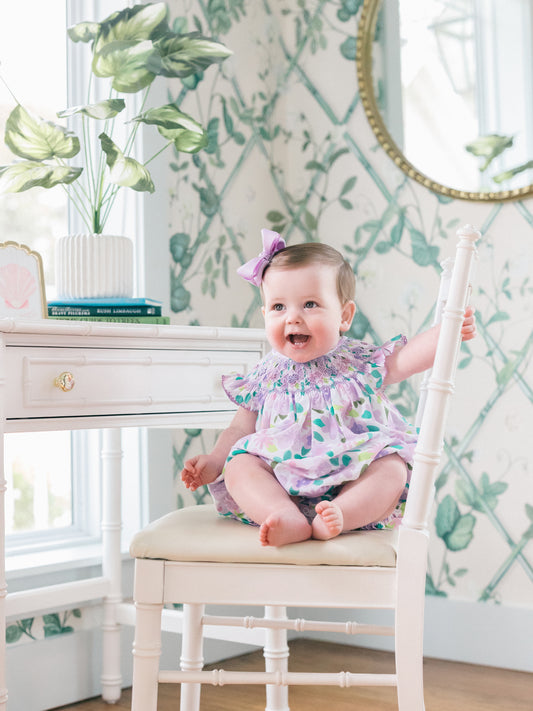 Baby sitting on a chair in a room with decorative wallpaper and a mirror.