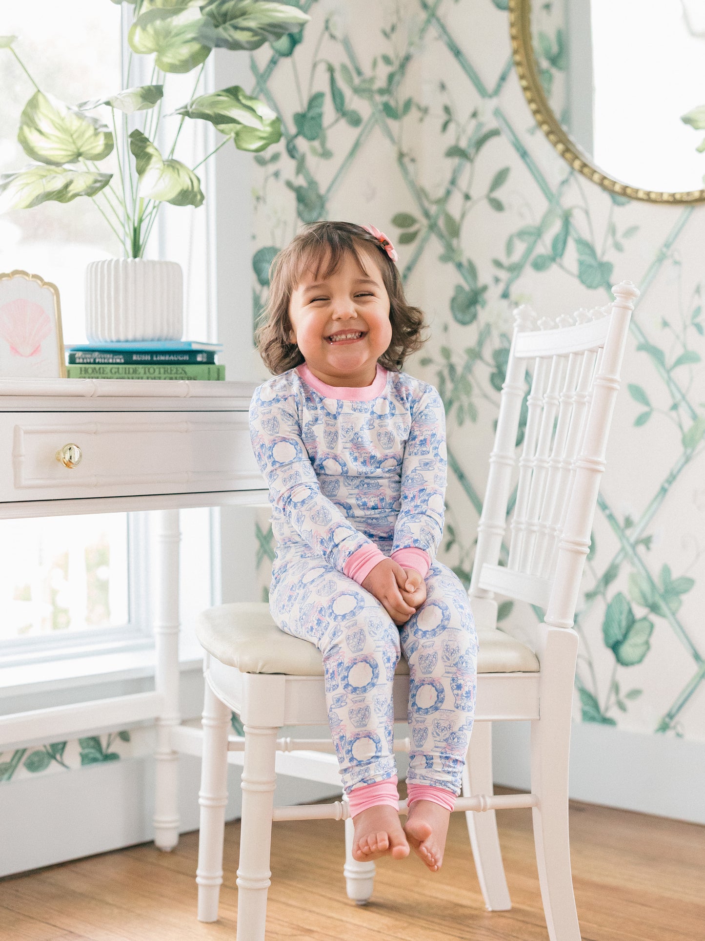 Child in pajamas sitting on a chair in a room with floral wallpaper