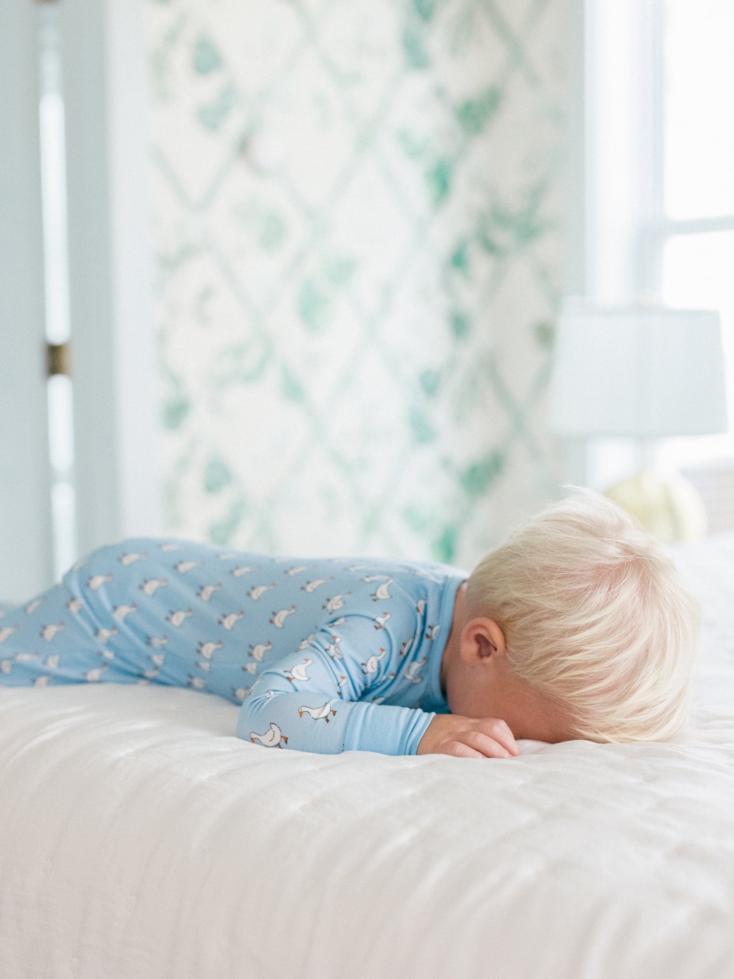 Child in blue pajamas lying on a white bed with a blurred background