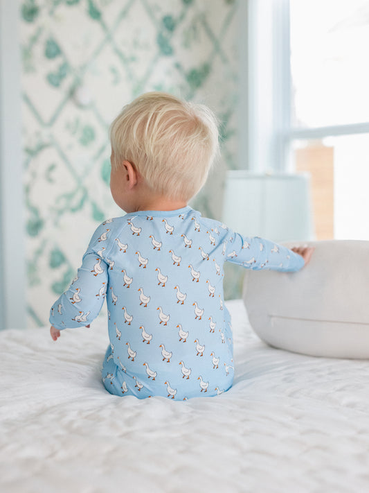 Child wearing a blue onesie with duck pattern sitting on a bed.