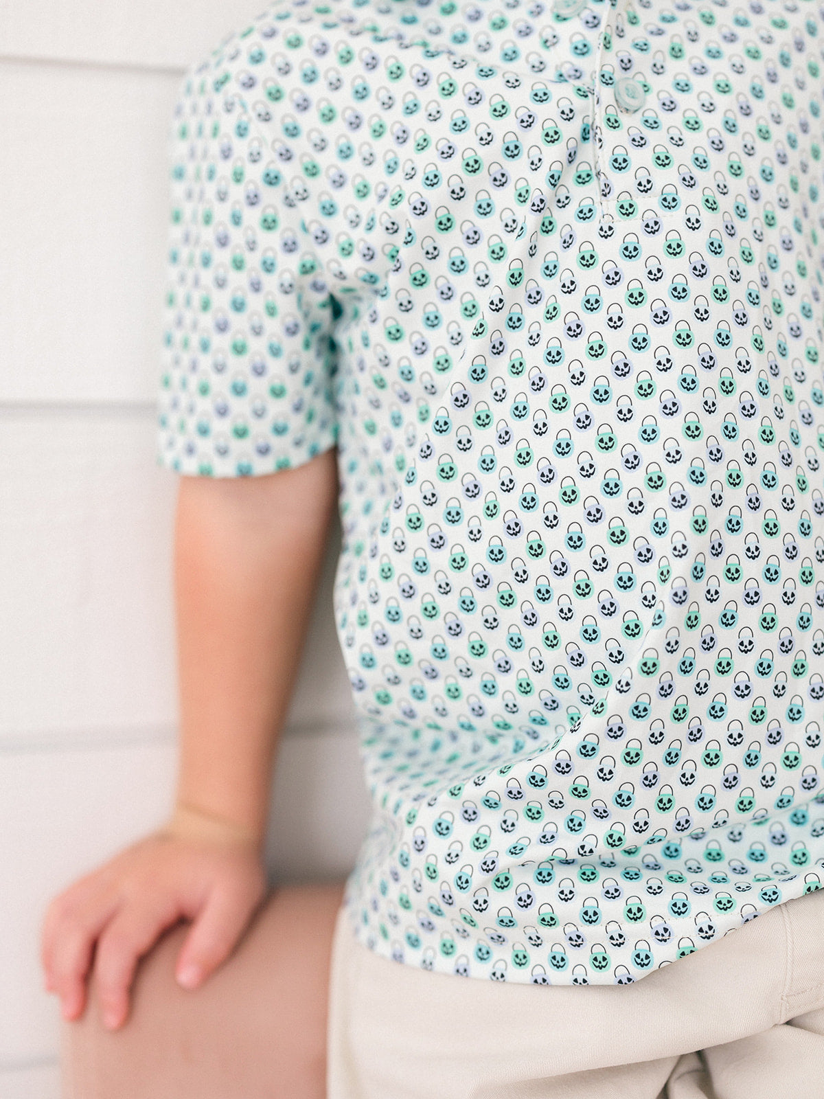 A little boy wearing a green and blue Halloween bucket print with blue buttons