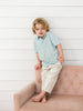A little boy wearing a green and blue Halloween bucket print with blue buttons