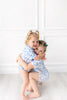 Two young girls in matching blue floral outfits hugging against a white wall.