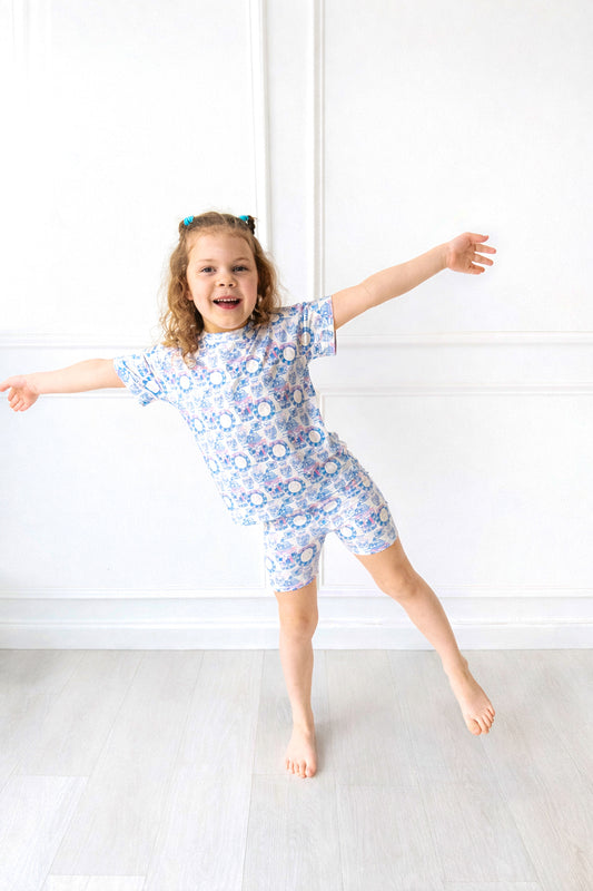 Child wearing a blue floral outfit standing on a white floor with a white wall background