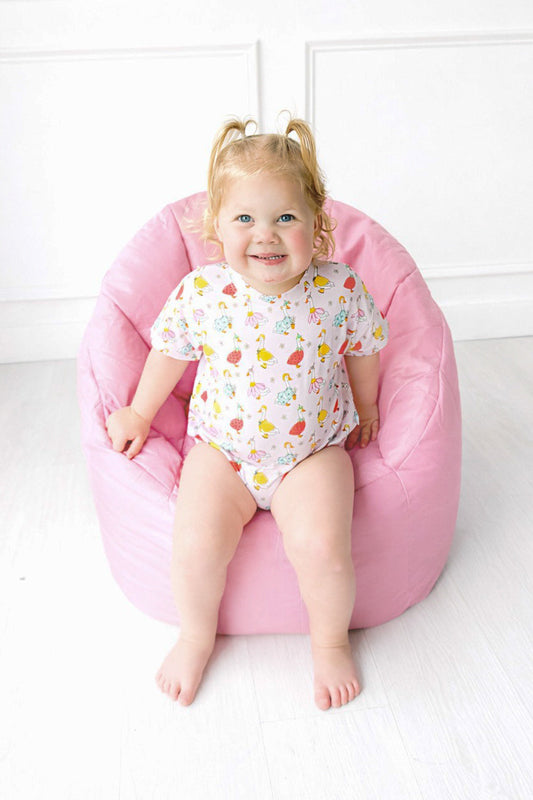 Child sitting on a pink bean bag chair against a white wall