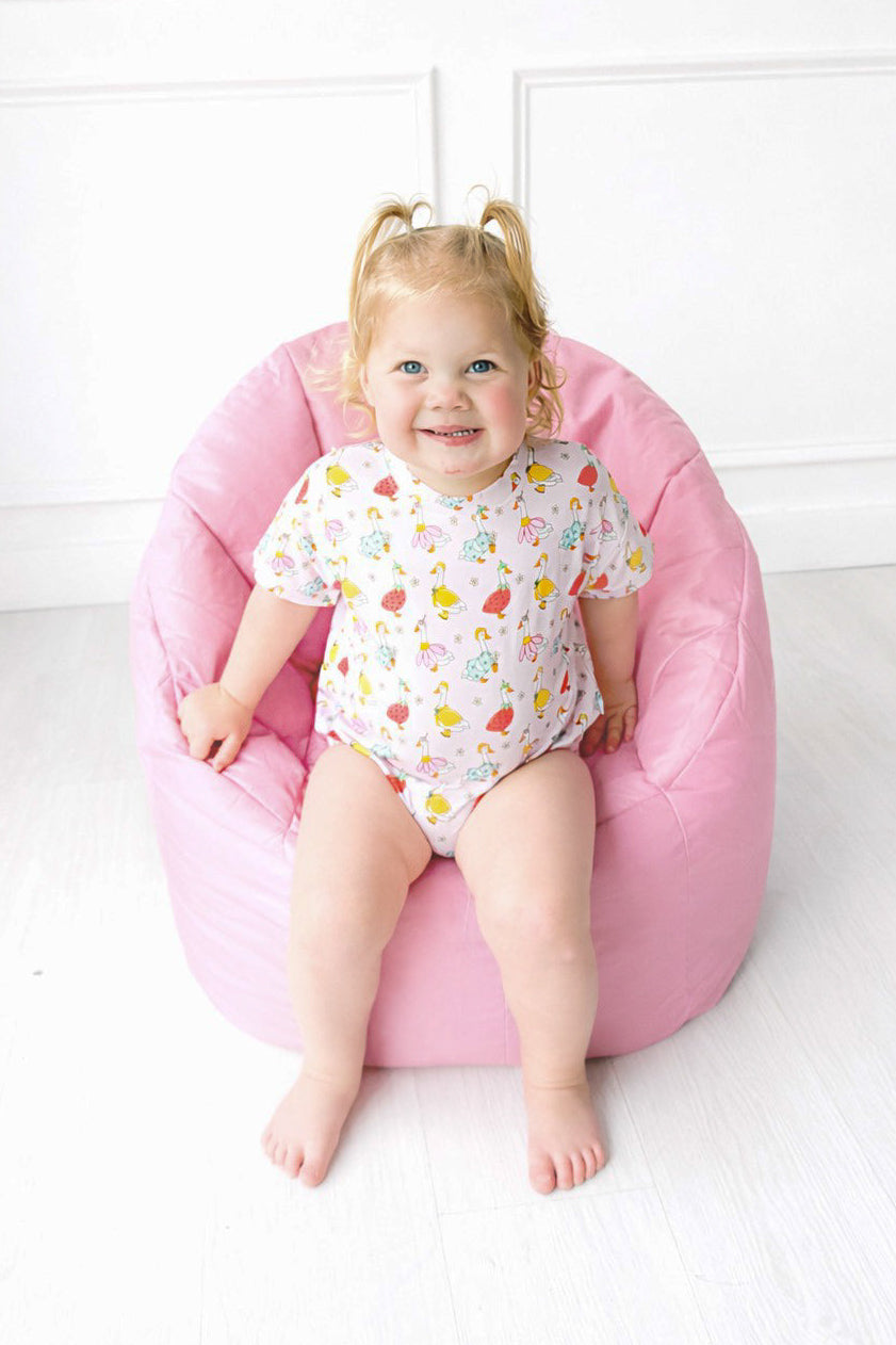 Child sitting on a pink bean bag chair against a white wall