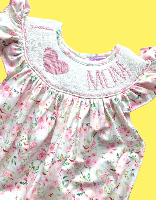 Close up of pink floral smocked outfit with "I [heart] MOM" handstitched on smock plate with pink lettering